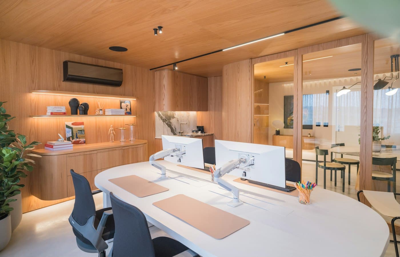 Un bureau contemporain lambrissé de bois clair, deux écrans sur une grande table blanche