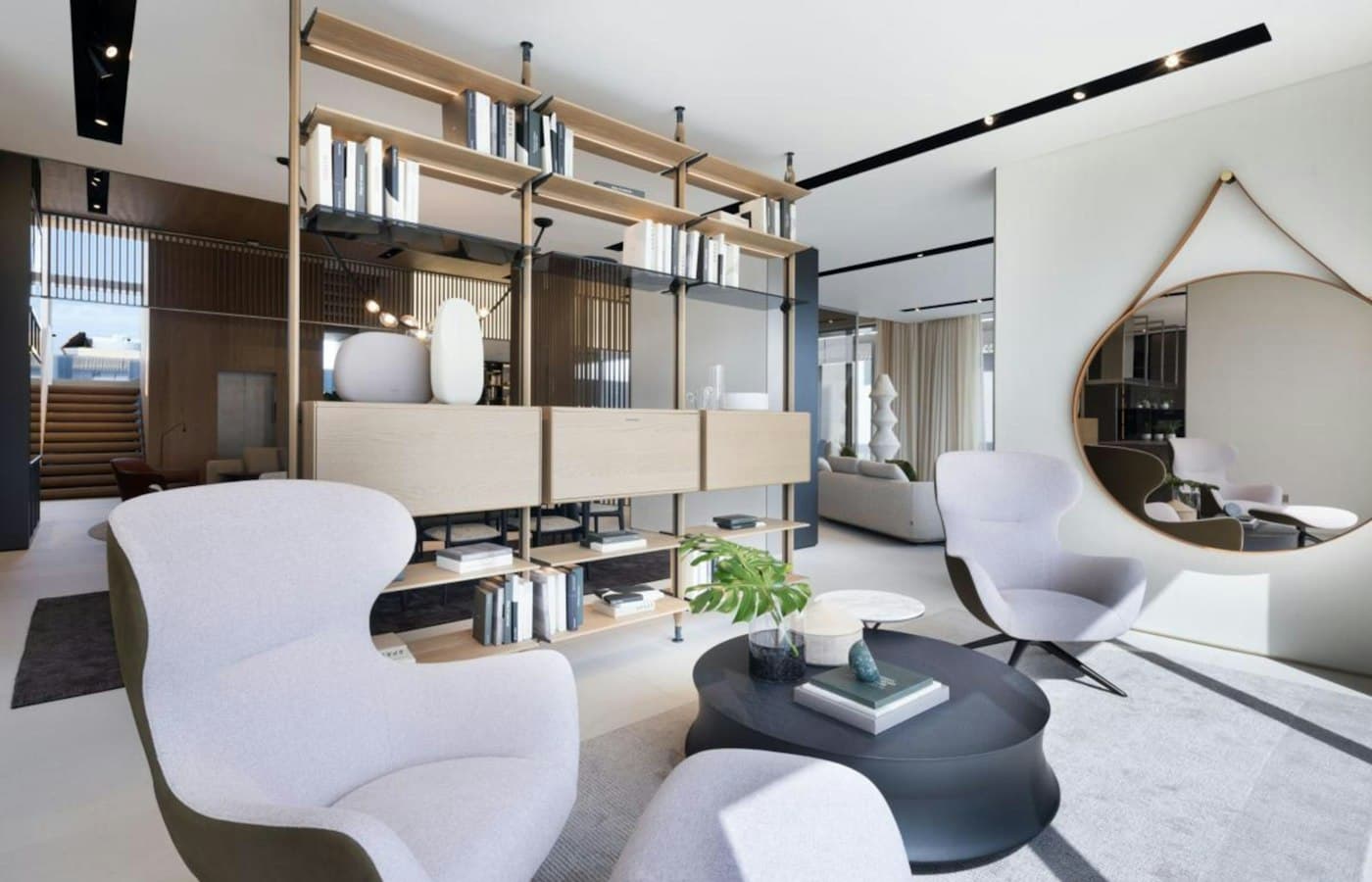 Un salon d’accueil clair, deux fauteuils enveloppants et un grand miroir rond au mur