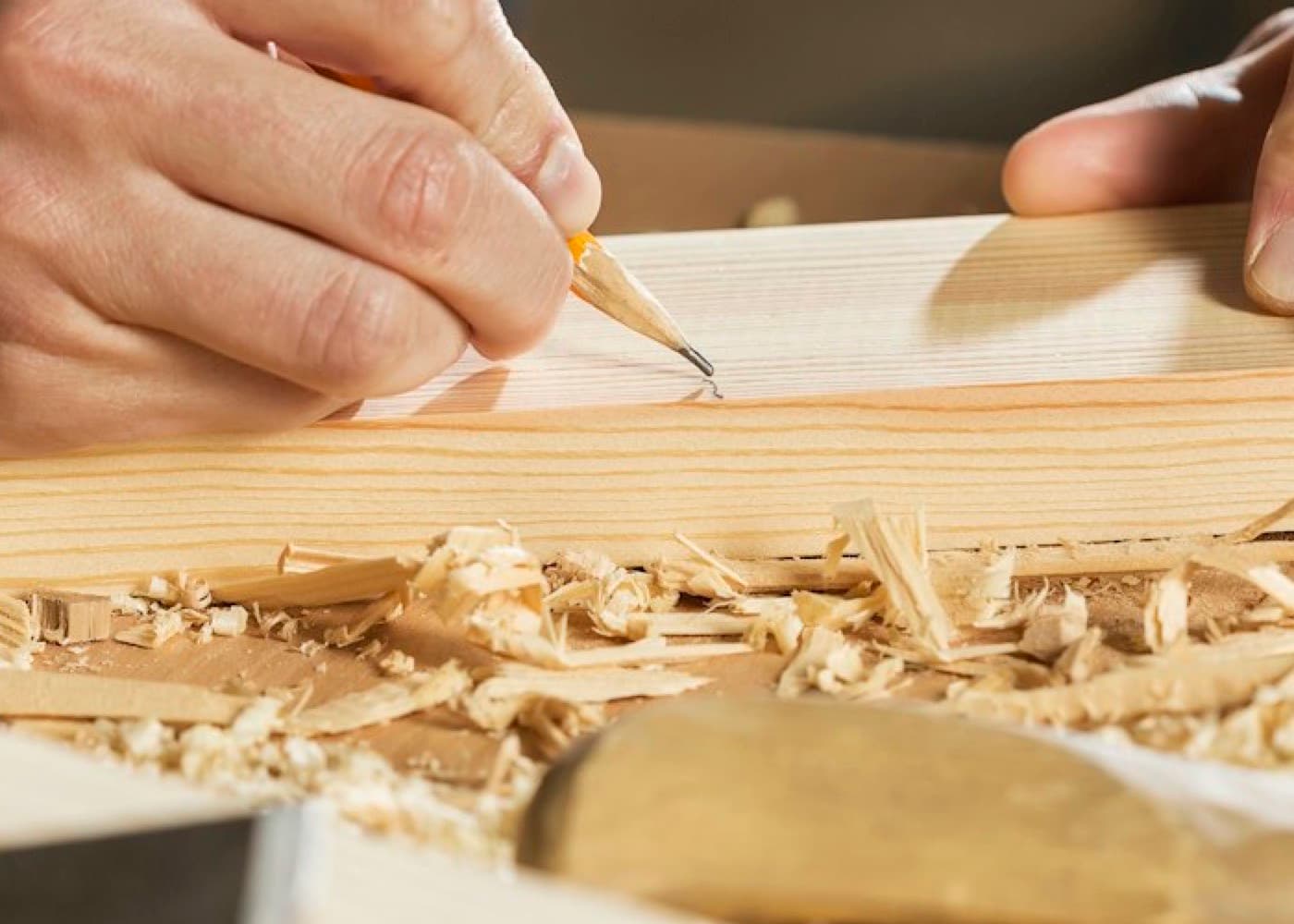 Un artisan trace un repère au crayon sur une planche de bois dans son atelier